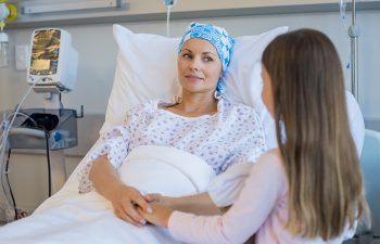 Mother fighting with cancer in conversation with daughter while resting on hospital bed. Young woman with tumor feeling good on meeting her little girl in hospital. Woman receiving cancer chemotherapy.